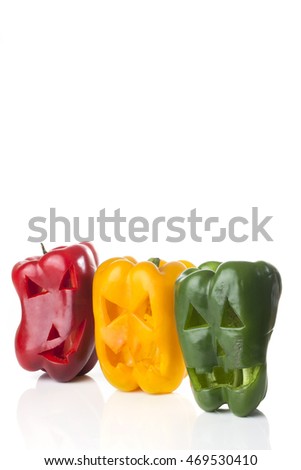 Food art creative concept. Halloween scary faces carved into green,  red and yellow capsicum vegetables isolated over a white background.