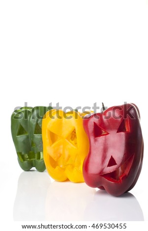 Food art creative concept. Halloween scary faces carved into green,  red and yellow capsicum vegetables isolated over a white background.