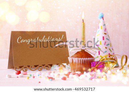 Birthday concept with cupcake and candle next to greeting card on wooden table. Selective focus. Glitter overlay
