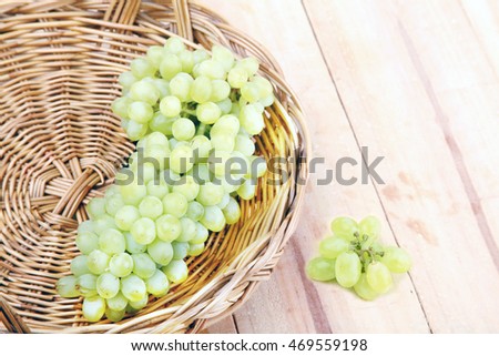 Bunch of grapes with green vine leaves in basket on wooden table .