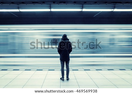 Lonely young man shot from behind at subway station with blurry moving train in background Royalty-Free Stock Photo #469569938
