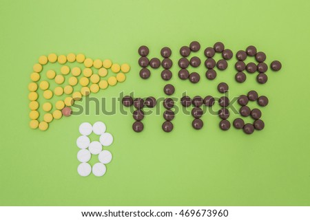 Figure or shape (contour) of human liver, composed of yellow tablets, and the diagnosis of hepatitis B sign made of yellow and white pills or tablets on a green paper background. Idea for hepatology