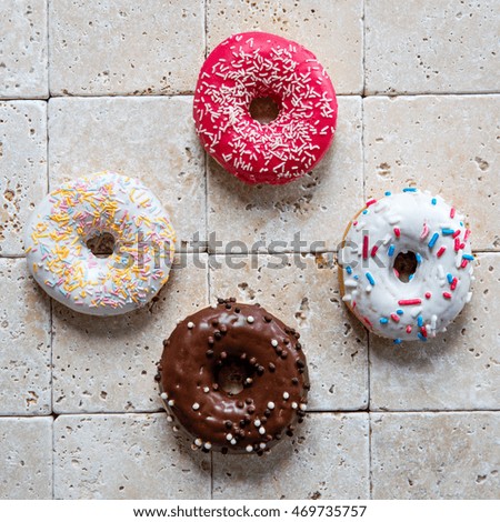 top view of four colorful sugar coated donuts for concept of fun, geometry and shape in dessert and sweets over pure limestone background, design flat lay