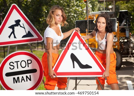 Two women in orange overalls are mounting " No Men" signs on the road.