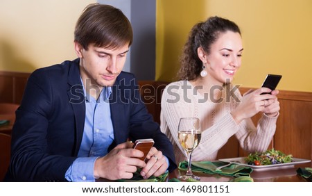 smiling young man sitting with his wife at restaurant table with smartphones. focus on man