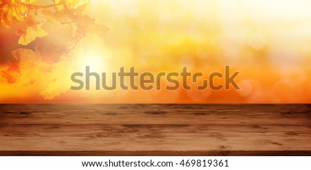 Empty wooden table in front of a autumn background in orange and gold tones