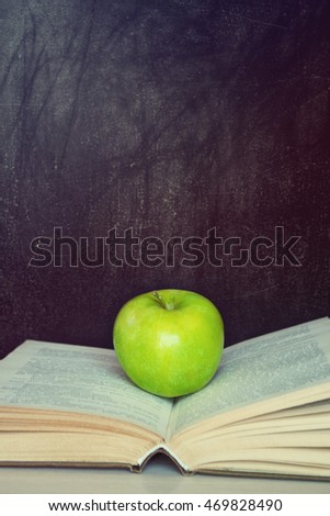 Apple resting on the book with chalk board as background.Back to school.