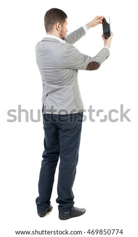 back view of standing business man photographing a phone or tablet. Rear view people collection.  backside view of person.  Isolated over white background. The bearded man in a gray jacket photographs