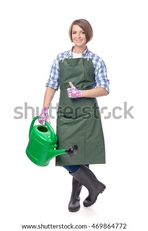 pretty smiling woman gardener in gloves and apron with watering can showing thumb up isolated on white background. proposing service. advertisement gesture. business, gardening and floristry concept 
