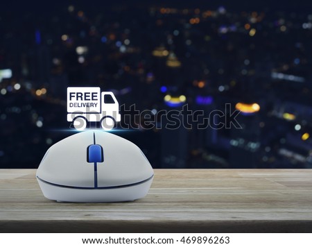 Wireless computer mouse with free delivery truck icon on wooden table over blur light city tower, Transportation business concept