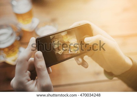 people and technology concept - close up of hands with smartphone picturing beer at bar