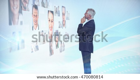Thoughtful businessman looking at a wall covered by profile pictures on white background