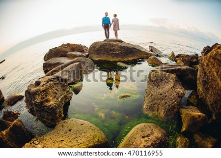 Rounded picture of the couple standing on the stones by the sea
