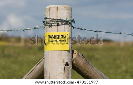 Barbed wire agricultural fencing with an electric fence warning sign.