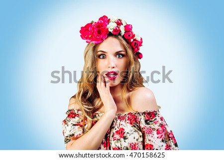 pretty young woman ( girl ) in wreath with flowers smiling and surprised on blue white  background