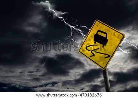 Slippery when wet road sign against a stormy background with lightning and copy space. Dirty and angled sign adds to the drama.