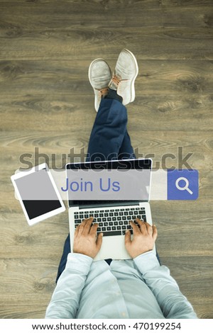Young man sitting on floor with laptop and searching JOIN US concept on screen