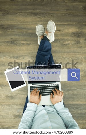 Young man sitting on floor with laptop and searching CONTENT MANAGEMENT SYSTEM concept on screen