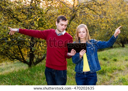 Young tourists couple man and woman pointing in opposite directions holding map on the tablet and planning trip or get lost in the woods. Traveling concept