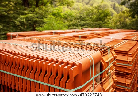 Stacks of red tiles associated with warehousing and transportation, to build a house. The roof of a modern tiled roof covering the house. Tile on the building pallets stacked in standard packaging