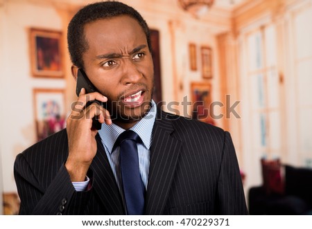 Handsome man wearing business suit talking on mobile phone, as seen from front angle, lobbby background
