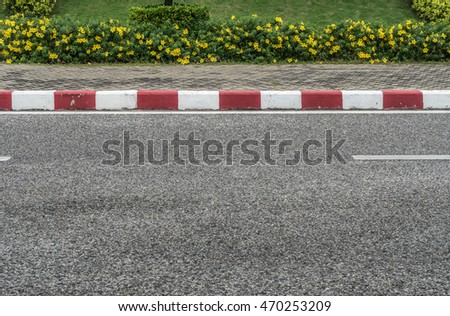 Asphalt road with red and white concrete curb and yellow flowers