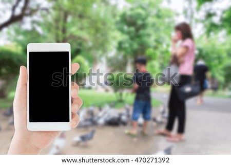 woman use mobile phone and blurred image of a boy feeds pigeons with his mother in the park