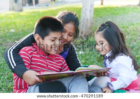 Three latin children reading a book in the park Royalty-Free Stock Photo #470291189