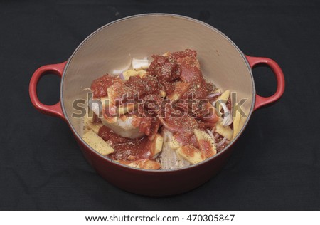 Potatoes, onions and tomato in th red saucepan. black background