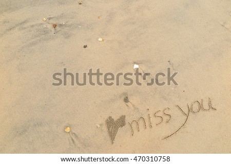 written words "miss you" on sand of beach