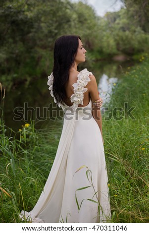 Portrait of a beautiful young bride wearing a slinky dress on the bank of the river in foliar summer forest