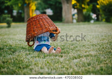 A child hides in a basket on the grass in the park