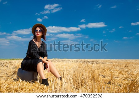 photo of the beautiful young woman sitting on the suitcase in the field