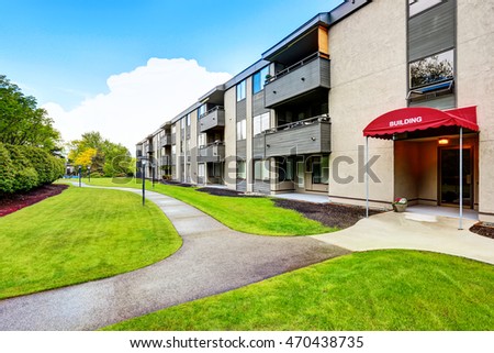 Large beige apartment building with three floors and balconies. Well kept lawn. Northwest, USA.