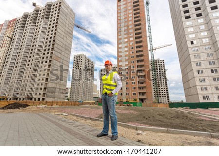 Photo of young construction engineer standing in front of buildings under construction