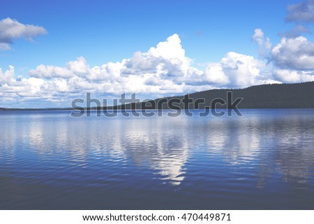 Beautiful summer day in Finland. An image of big lake and deep blue sky with cloud formations. Some hills are in the background. Image has a vintage effect applied.