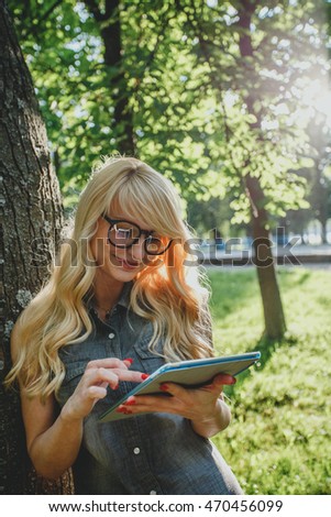 Happy young blonde woman using tablet pc in the park