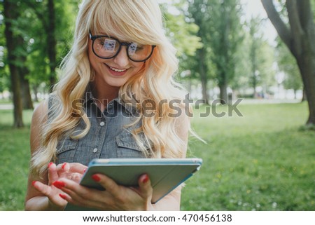 Happy young blonde woman using tablet pc in the park