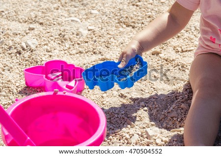 Little kid sitting on the sand and playing with plastic toys. Travel photo of girl on the beach. Summer vacation in Croatia.