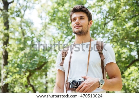 Attractive young man with backpack and old photo camera standing in forest