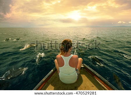 Young traveler sitting on the boat and filmed a flock of dolphins