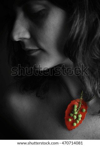 B&W photo of a beautiful women with colored organic green berries necklace on a bed of red leaf