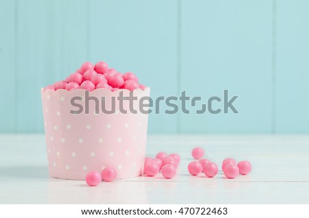 Pink candies in pink paper cup on white and blue wooden background - Pink bubblegum and candy Royalty-Free Stock Photo #470722463
