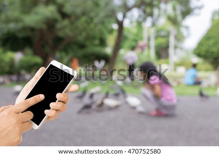 woman use mobile phone and blurred image of a child is feeding pigeons , some people are in the park