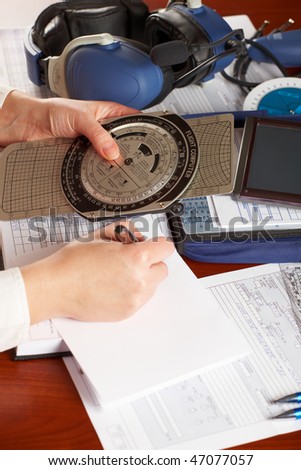 Pilot equipment with airplane pilot hands doing calculations, other tools like flight computer used for aviation calculations, protractor, kneepad with charts and professional headset