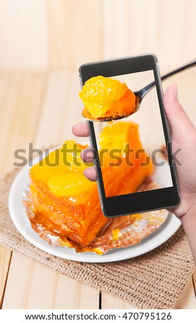 Hand with smart phone shooting image on orange fruit cake