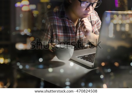 Young businessman working on office at night and using notebook analyze online business information, holding cup espresso, blurred background. Horizontal, film effect, Blur night city light bokeh.
