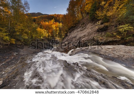 The cascade of the mountain river flowing through a forest colorful autumn.Long exposure
