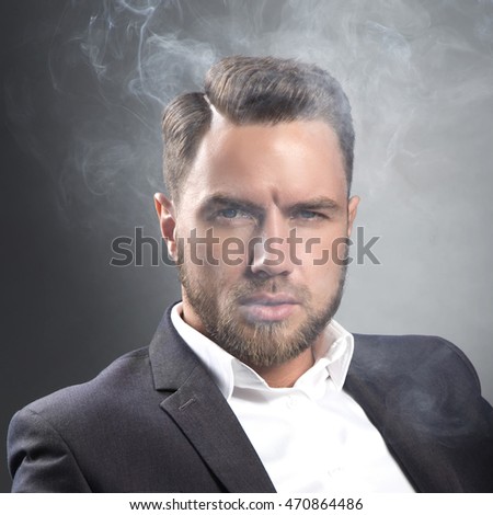 Young handsome bearded caucasian man. Perfect skin and hairstyle. Wearing grey suit. Studio portrait on gradient black to grey background.