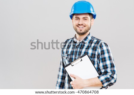 Man in checked T-shirt and blue building helmet looking at camera and smiling. Holding tablet. Building concept, builder. Indoors, studio, waist up